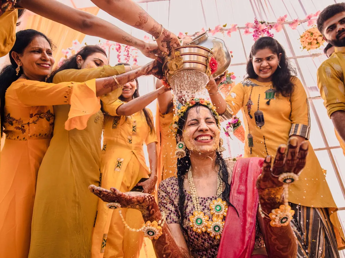 Bride laughing as family in yellow pour water over her at the haldi