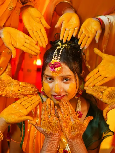 Smiling bride with turmeric on her face, surrounded by haldi-stained hands