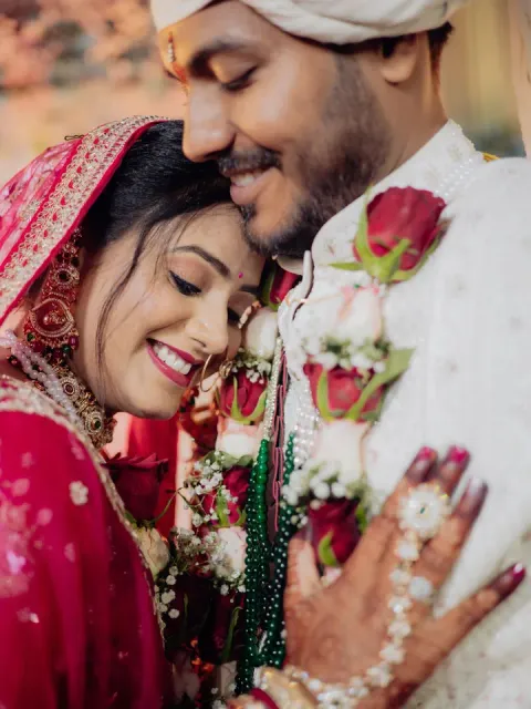 Smiling bride leaning into the groom, who wears an ivory sherwani and rose garland