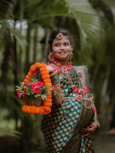 Smiling pregnant woman in a green silk saree and floral jewellery holding a flower basket
