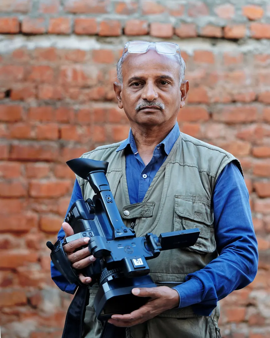 Grey-haired photographer in a khaki vest holding a professional camera